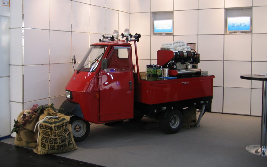 12 kleine rote Piaggio-Espressobar für Standcatering auf einem Stand in Messehalle