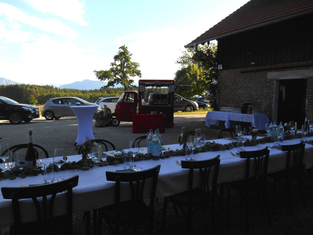 41 rote Piaggio Ape mit Barista Ausstattung davor ein langer eingedeckter Tisch für eine Feierlichkeit