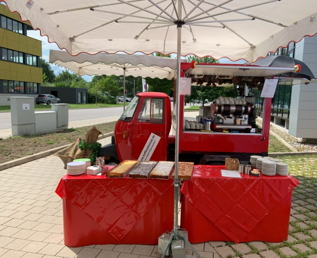 50 italienisches Kaffeedreirad, davor Tisch mit Blechkuchen Geschirr und Hafermilch